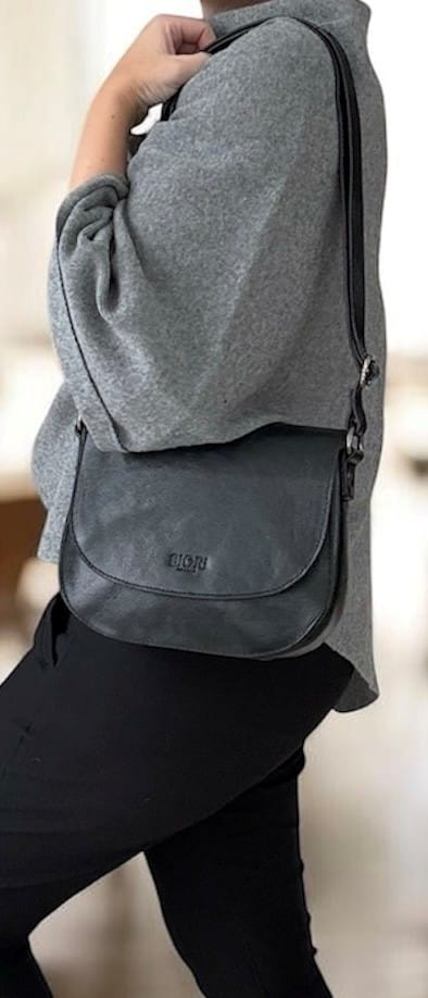 Handväska i svart skinn med en rundad klaff och en justerbar axelrem från Biori Sweden, buren av modell